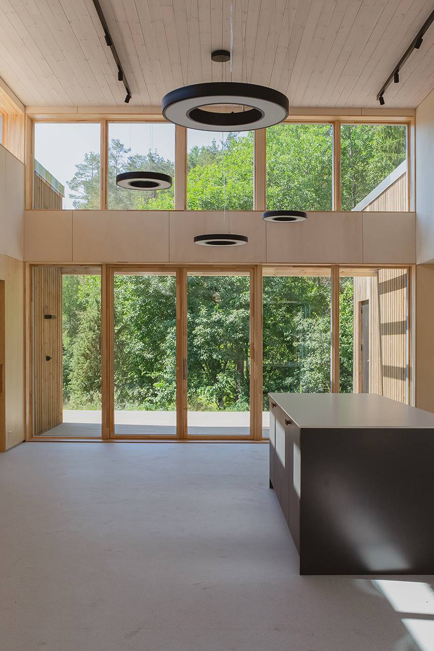 Moderne interiør med dobbel takhøyde, store vinduer mot skogen og elegant mørkt kjøkken